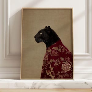 May include: Framed art print featuring a black panther wearing a red floral patterned robe. The panther is in profile against a neutral background. The frame is a light wood color, adding a touch of elegance to the artwork.