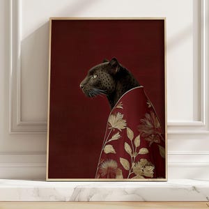 May include: A framed art print featuring a black panther wearing a red and gold floral patterned garment. The panther is depicted in profile against a deep red background. The artwork is displayed in a room with white molding.