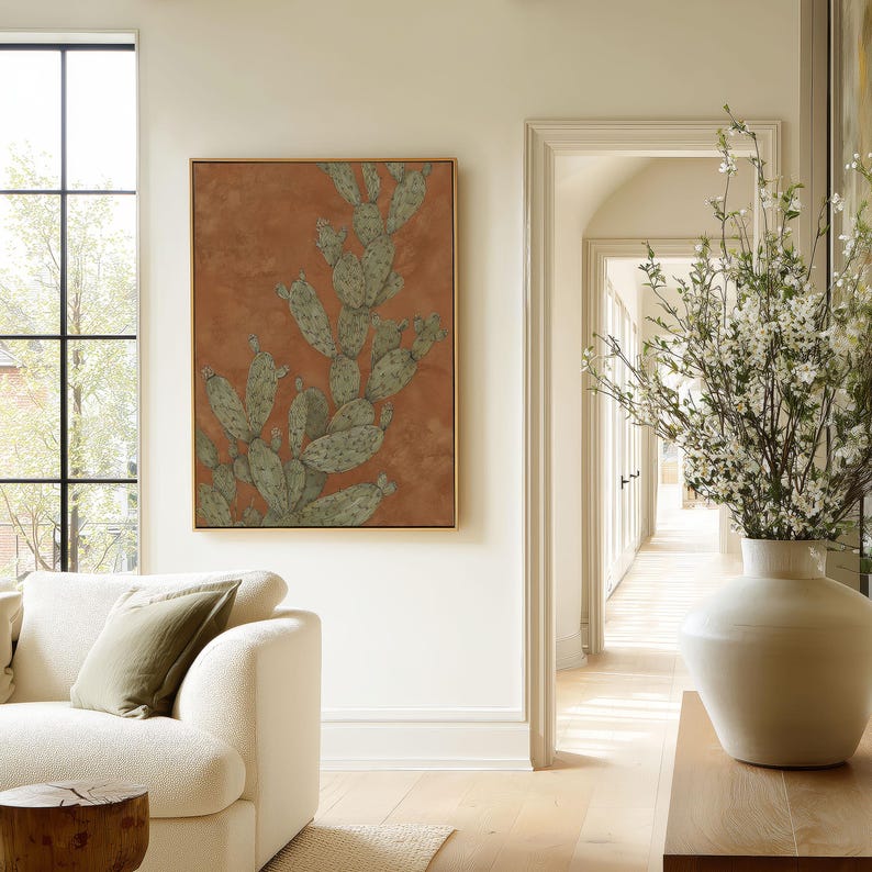 Botanical prickly pear cactus in green and warm brown, rustic vintage mood, presented as a framed poster in an airy living room near an archway.