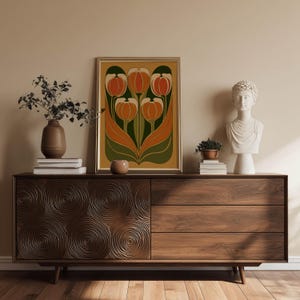 Decorative vintage tulip design in orange and deep green tones wall art print resting on a mid century sideboard styled with sculptural decor and books.