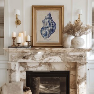Ornate framed vintage seashell poster in deep blue on ivory-beige paper centered above a marble fireplace styled with candles and decorative vases.
