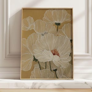 May include: A framed art print of white flowers with detailed line work against a mustard yellow background. The flowers have red centers and are set in a light brown wooden frame. The artwork is displayed on a white marble surface.