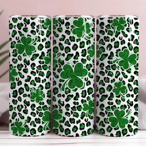 May include: Three stainless steel tumblers with a white background, green leopard print, and green glitter shamrocks. The tumblers are cylindrical and feature a St. Patrick's Day theme.