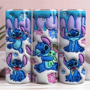 May include: Three stainless steel tumblers featuring the character Stitch from Lilo & Stitch. The tumblers have a white base with blue Stitch illustrations, purple accents, and a blue and purple drip design. Pink and blue floral accents complete the design.
