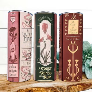 May include: Three insulated tumblers with book-themed designs. The tumblers feature titles like "A Court of Thorns and Roses," "A Court of Mist and Fury," "A Court of Wings and Ruin," and "A Court of Silver Flames." Each tumbler has a different color scheme and floral illustrations.