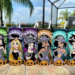 May include: Six colorful tumblers with white straws, featuring Disney princess illustrations in witch costumes. Each tumbler has a Starbucks logo and a pumpkin at the base. The tumblers are arranged on a stone surface near a pool.