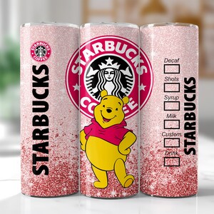 May include: A pink glitter Starbucks tumbler featuring Winnie the Pooh. The tumbler has the Starbucks logo and text. The design includes a drink customization chart. The tumbler is cylindrical and has a pink glitter gradient.
