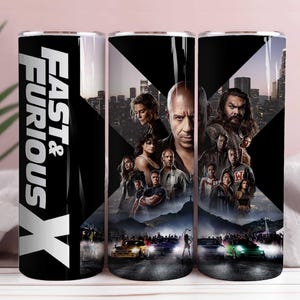 Può includere: Un bicchiere in acciaio inossidabile con un design del film Fast & Furious X. Il bicchiere ha uno sfondo nero con il titolo del film in bianco e immagini del cast. Il design include auto e paesaggi urbani.