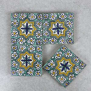 Puede incluir: Cuatro baldosas de cerámica cuadradas con fondo turquesa y un patrón repetitivo de estrellas y flores en amarillo, azul y blanco. Una baldosa está en ángulo, mostrando el patrón desde una perspectiva diferente.