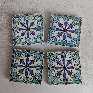 May include: Four square ceramic tiles with a repeating floral design. The tiles feature a white background with a central blue flower, surrounded by teal and black decorative elements. Each tile is approximately 4 inches square.