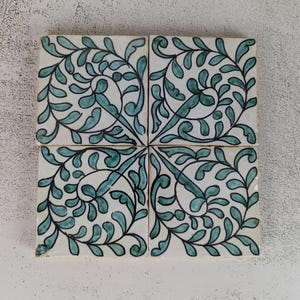May include: Four square ceramic tiles with a white background and a teal and black leaf design. The tiles are arranged together, forming a larger square. The leaf pattern is symmetrical and detailed.