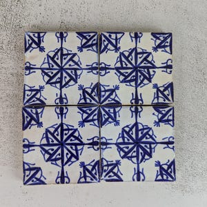 May include: Six square ceramic tiles arranged in a grid. Each tile features a white background with a repeating blue geometric starburst pattern. The tiles are likely for decorative use in a kitchen or bathroom.