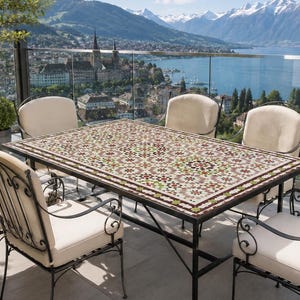 May include: A rectangular outdoor dining table featuring a multi-colored geometric mosaic tile top and a black metal frame, accompanied by four matching black metal chairs with cream-colored cushions, arranged on a balcony overlooking a lake.