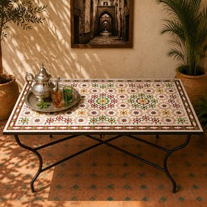 May include: A rectangular table with a mosaic tile top featuring a geometric pattern in white, green, red, and yellow. The table has a black metal frame with curved legs and a cross-brace. A silver teapot and two glasses sit on a metal tray.