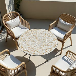 Op de afbeelding: Buitenpatio set met een ronde tafel met een mozaïek tegelblad in beige en crèmetinten. Vier rotan stoelen met witte kussens en kussens omringen de tafel, waardoor een gezellige zithoek ontstaat.
