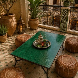Puede incluir: Una mesa de centro rectangular con superficie de azulejos verdes y patas de metal negro, rodeada por cuatro pufs redondos de cuero marrón. Sobre la mesa hay una bandeja de metal plateado con una tetera plateada y tres vasos de té coloridos.