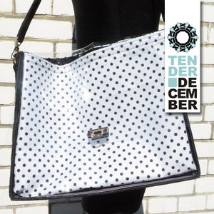 Può includere: Una grande borsa tote bianca con pois neri e un pannello frontale in plastica trasparente. La borsa ha una tracolla nera e una chiusura argentata.