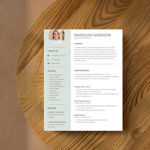 May include: A resume with the name MARCELINE ANDERSON, Digital Marketing Manager, displayed on a white background. The resume includes sections for contact information, skills, work experience, and education. The resume is on a wooden surface.