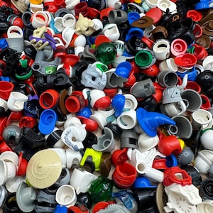 Può includere: Una collezione di caschi e copricapi giocattolo in plastica colorata di varie forme e dimensioni. L'assortimento comprende pezzi rossi, bianchi, blu, neri e grigi, alcuni con visiere e design unici. Sono visibili vari accessori per giocattoli.