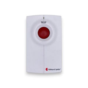 Op de afbeelding: Een wit rechthoekig apparaat met een rode ronde knop in het midden. Het woord "TEST" staat boven de knop gedrukt. Het apparaat heeft het logo "Bellman & Symfon" rechtsonder.