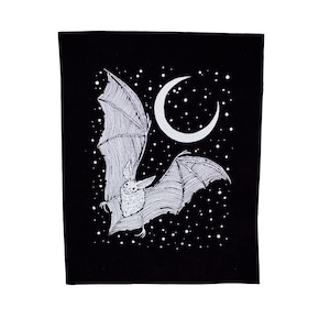 May include: A black fabric patch with a white outline of a bat flying in front of a crescent moon and a starry night sky.