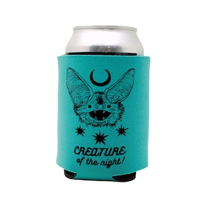 May include: A turquoise blue can cooler with a black and white illustration of a bat with a crescent moon and stars. The text "CREATURE of the night!" is printed on the cooler.
