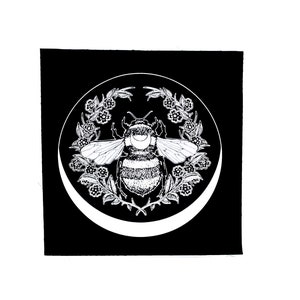 May include: Black and white illustration of a bee with a crescent moon on its back, surrounded by a wreath of flowers.