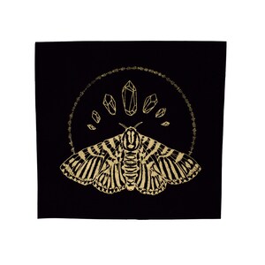 May include: A gold foil print of a moth with geometric wings and a circle of crystals above it on a black background.