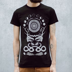 May include: Black t-shirt with a white graphic design featuring a circle with moons, a skull, and snakes. The design is centered on the shirt.