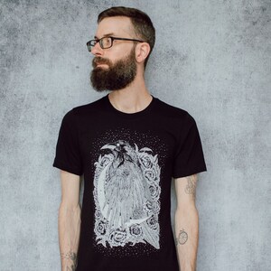 A unisex black t-shirt with a white hand screen printed design. The detailed hand drawn natural illustration is of a raven against a large crescent moon and peony flowers over a starry sky.