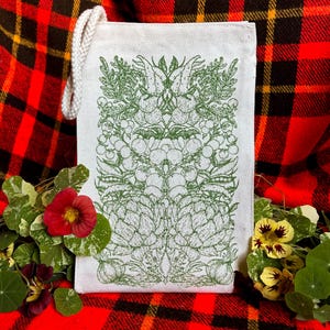 A natural colored canvas lunchbag featuring hand drawn art of various vegetables including artichokes, radishes, tomatoes, peas, chanterelle mushrooms, and garlic. The design is screen printed in warm green pink on the front of the bag.