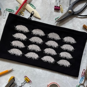 May include: A black rectangular zipped pouch featuring a repeating white embroidered pattern of woodlice. The pouch is constructed from fabric and includes a black zip closure along the top edge, showcasing a detailed insect motif.