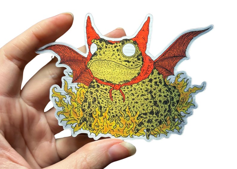 A die cut brushed silver metallic sticker of a full color toad in a devil costume with wings and flames.