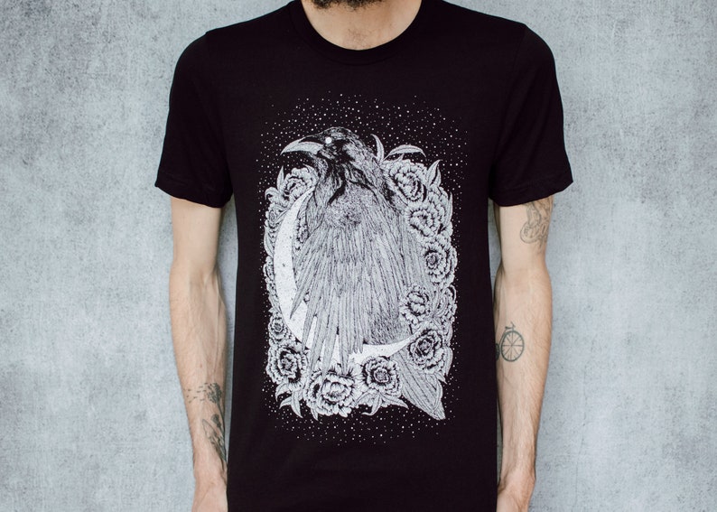 A unisex black t-shirt with a white hand screen printed design. The detailed hand drawn natural illustration is of a raven against a large crescent moon and peony flowers over a starry sky.