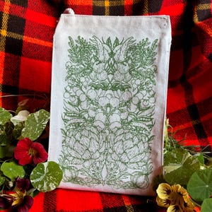 A natural colored canvas lunchbag featuring hand drawn art of various vegetables including artichokes, radishes, tomatoes, peas, chanterelle mushrooms, and garlic. The design is screen printed in warm green pink on the front of the bag.