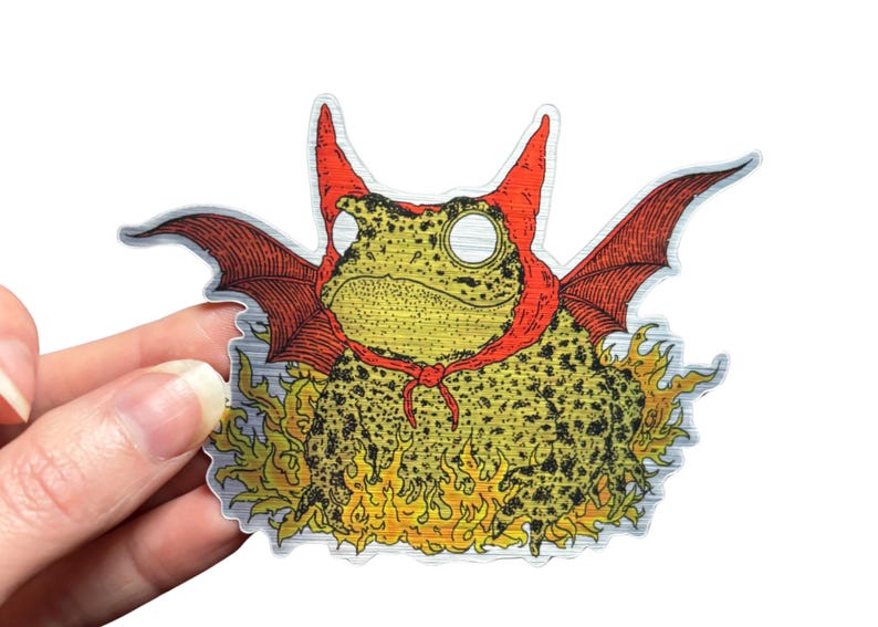 A die cut brushed silver metallic sticker of a full color toad in a devil costume with wings and flames.
