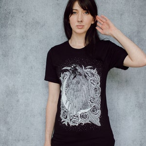 A unisex black t-shirt with a white hand screen printed design. The detailed hand drawn natural illustration is of a raven against a large crescent moon and peony flowers over a starry sky.