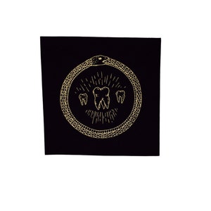 May include: A black square with a gold snake design. The snake is curled into a circle and has a tooth in its mouth. There are three teeth in the center of the circle.