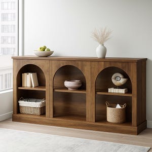 May include: A wooden bookshelf with three arched openings. The shelves display decorative items like books, a vase, a bowl, and a woven basket. The bookshelf is made of wood and has a warm, natural finish, suitable for living room or home decor.
