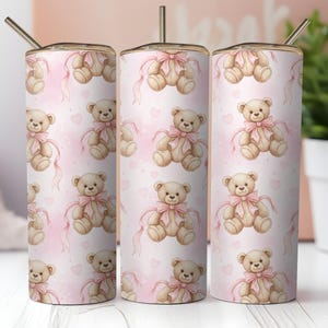 May include: Three 20 oz. stainless steel tumblers with a repeating pattern of watercolor teddy bears wearing pink bows on a pink background with hearts. Each tumbler has a gold-colored straw.