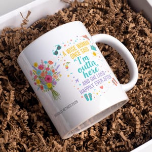 Op de afbeelding: Witte keramische mok met een boeket kleurrijke bloemen en de tekst "Een wijze vrouw zei ooit 'Ik ben hier weg' en ze leefde nog lang en gelukkig." De mok heeft ook de tekst "Officieel Gepensioneerd 2026."