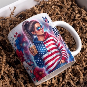 May include: White ceramic mug featuring a graphic of a woman wearing sunglasses and a hoodie with an American flag design. The mug has a white handle and is decorated with flowers and butterflies. The word "AMERICA" is visible on the mug.