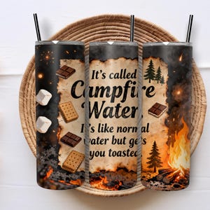 May include: Three stainless steel tumblers with black straws, featuring a campfire theme. The design includes text that reads "It's called Campfire Water," along with images of marshmallows, graham crackers, chocolate, and a campfire.