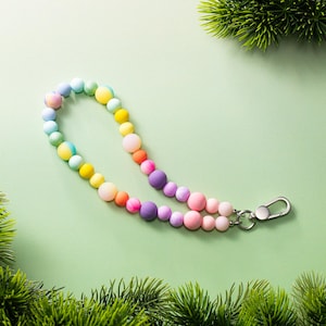 May include: A wristlet lanyard composed of a single strand of smooth, round silicone beads in a vibrant rainbow gradient of colors including yellow, orange, pink, purple, blue, and green, finished with a silver-toned metal lobster clasp.