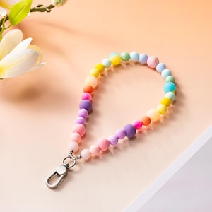 Puede incluir: Un llavero de pulsera que presenta una disposici&oacute;n circular de cuentas de silicona con acabado mate suave en un degradado de arco&iacute;ris vibrante de rosa, morado, naranja, amarillo, verde y azul, unido a un cierre de mosquet&oacute;n de metal plateado.