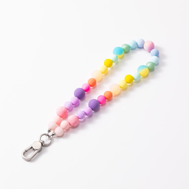 Puede incluir: Un llavero de mu&ntilde;eca con un bucle de cuentas de silicona de acabado mate y suave en un vibrante degradado arco&iacute;ris de rosa, morado, naranja, amarillo, verde y azul, unido a un mosquet&oacute;n de metal plateado para una sujeci&oacute;n segura.