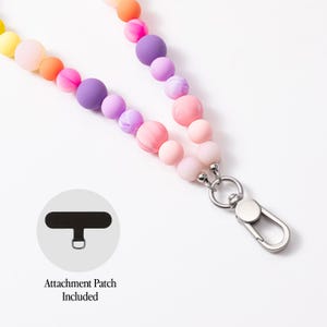 Puede incluir: Un cord&oacute;n con una hilera de cuentas de silicona multicolor en tonos amarillo, naranja, rosa y morado, unido a un mosquet&oacute;n de metal plateado. Se incluye un parche de fijaci&oacute;n rectangular negro con una anilla de metal.