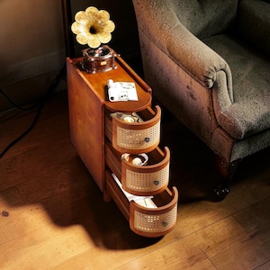Pode incluir: Uma mesa lateral de madeira com três gavetas com frentes de vime tecido. Um gramofone vintage com uma buzina de latão fica em cima da mesa. A mesa é de cor castanho quente e tem um design curvo.