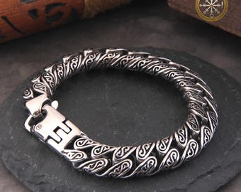Puede incluir: Una pulsera plateada con un diseño intrincado y estampado. La pulsera presenta una serie de eslabones interconectados, cada uno adornado con motivos estilizados y arremolinados. Un cierre resistente asegura la pulsera. El logotipo de The Vikings Amulet es visible en el fondo.
