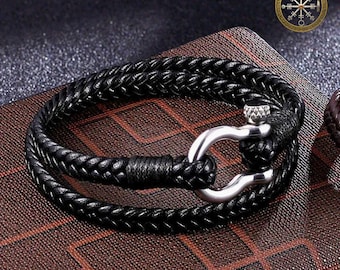May include: Black braided leather bracelet with a silver-colored clasp. The bracelet is made of two strands of braided leather and features a sturdy, industrial-style clasp. The Vikings Amulet logo is in the upper right corner.